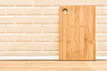 Bamboo wooden chopping board against white brick wall and kitchen countertop background. Light kitchen interior with workplace for cooking. Brown cutting board on table. Space for text