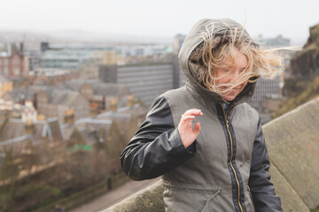 A young blonde woman's hair is blown in all different directions on a windy winter day in...