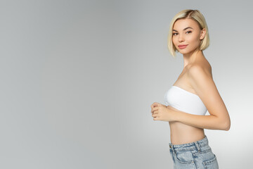 Blonde woman in white top looking at camera isolated on grey