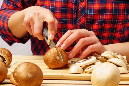 Close-up of the chef's hand cuts the forest mushroom champignon on the board .