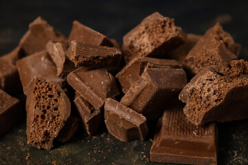 Different pieces of dark chocolate and cocoa powder on a dark surface.