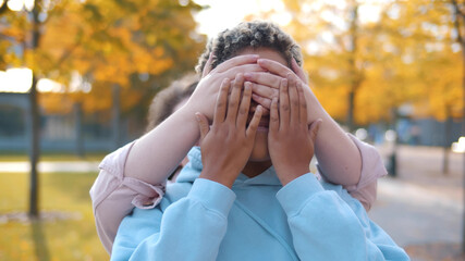 Woman closing eyes of her african girlfriend and kissing dating in autumn park