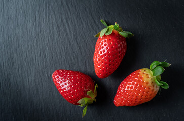 Fresh juicy strawberries, three pieces, close-upflat lay, on a marble stone background.