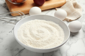 Fototapeta na wymiar Bowl with flour on white marble table, closeup. Cooking of delicious plum cake