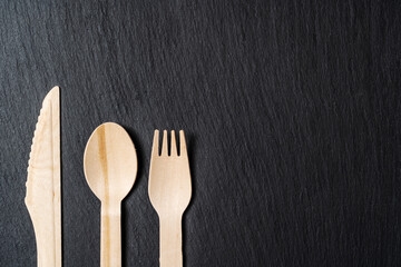 Disposable biodegradable tableware made of wood spoon, knife and fork on marble texture. Close-up.