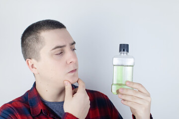 Fototapeta premium Close-up of a man in the bathroom using a mouthwash. Dental care concept. Procedure after brushing your teeth. Antibacterial mouth liquid. Pours, rinses and spits out liquid. Man look in the mirror