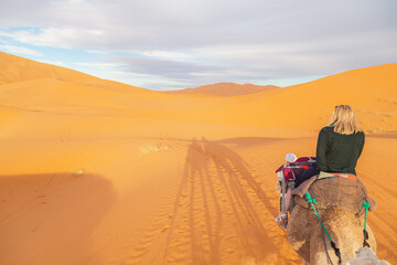 A young blonde female tourist on a camelback excursion along the desert sand dunes of Erg Chebbi near the village of Merzouga in southeastern Morocco.