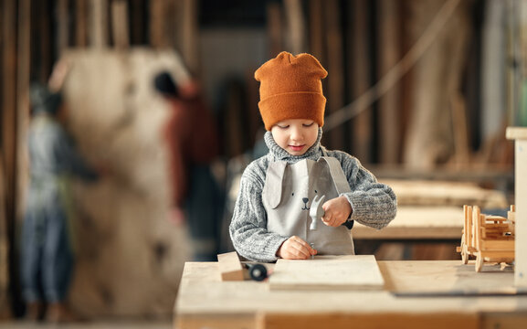 Kid with hammer making wooden detail with dad and mother in workshop