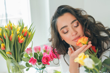 Emotional portrait of a young beautiful woman florist with dark curly hair, collects a bouquet of multicolored tulips. Small business. Spring holidays. Mothers Day. Women's Day.