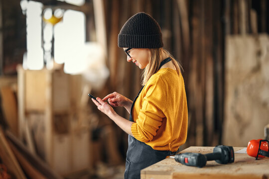 Female joiner using smartphone in workshop - Powered by Adobe