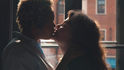 Couple of excited multiethnic lesbians kissing passionately in front of window
