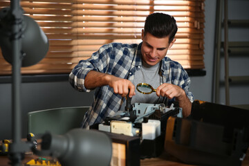 Repairman with magnifying glass and screwdriver fixing modern printer in office