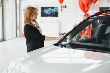 Young beautiful woman showing her love to a car in a car showroom