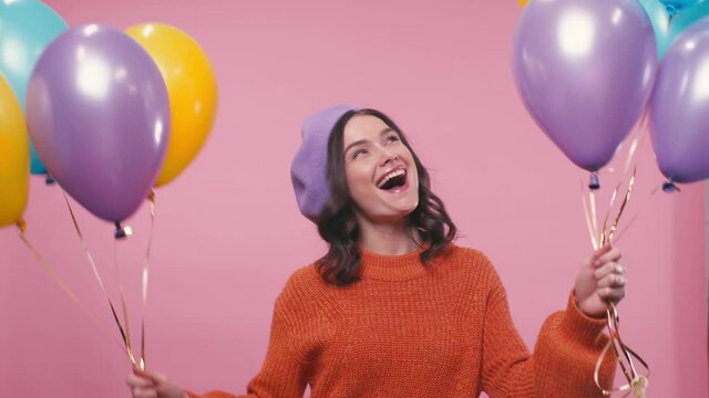 happy woman in beret holding colorful balloons isolated on pink