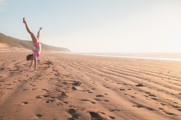 A young blonde female tourist does a cartwheel on the sand at Tafedna Beach in the province of Essouira, Morocco.