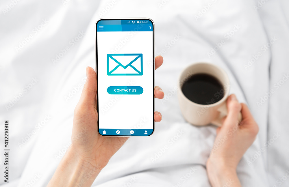 Poster lady sending e-mail message on cellphone lying in bed indoors