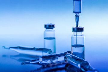 ampoule, glass vials and a medical syringe with a coronavirus vaccine on a blue background