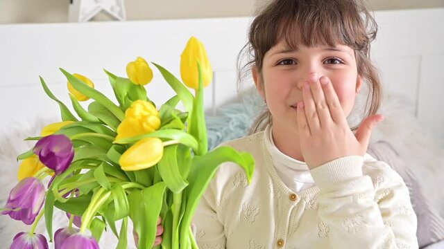 Lovely hugs of mom and daughter on a holiday for mother. Little girl gives a bouquet of bright tulips. Mother's Day or 8 March celebration concept. High quality FullHD footage