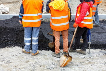 A team of road construction workers in orange overalls hold a meeting at a work site.