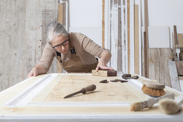 wood crafts, woman artisan carpenter works wood, sand an old door with sandpaper, with old handle...