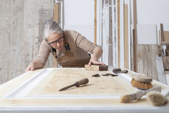 wood crafts, woman artisan carpenter works wood, sand an old door with sandpaper, with old handle tools in her workshop, restoration, diy and handmade works concept
