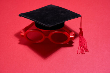 toy miniature maortarboard and red round glasses on red background
