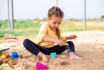 Little cute child girl sit on the sand and play with molds for sand. Ice-cream molds different...