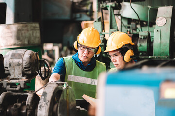 Work at factory.Two Asian workers man team working together in safety work wear with yellow helmet...