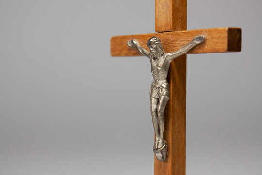 Horizontal close-up conceptual photography of a crucifix with a silver figurine of Jesus Christ on the wooden cross, against light grey background