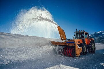 A snowplow truck removing snow from a winding rural road on sunny winter day. - obrazy, fototapety, plakaty