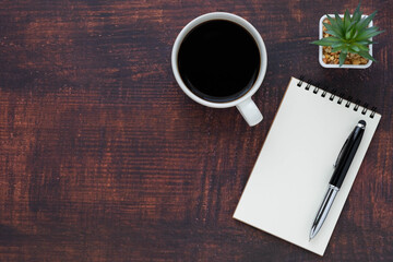 Top view of open school notebook with blank pages, coffee cup and pen for taking write notes on wood table background. Flat lay, creative workspace office. Business-education concept with copy space.