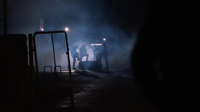 Wide shot of a group of men standing in the shadows in the night, dangerous criminals in smoke. Dangerous, urban scene.