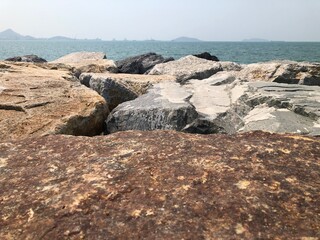 By the sea and the sea view, there are big rocks and sea waves hitting the rocks in the mist. Sea view and bright blue sky.
