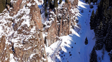 Freezing waterfall in the snowy mountains. View from the drone, from above. The rocks are covered with snow and ice. A small stream of water runs. The waterfall freezes. A group of people are resting