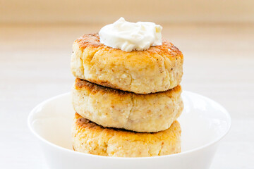 Homemade cottage cheese pancakes syrniki stack on round white bowl on white rustic table background
