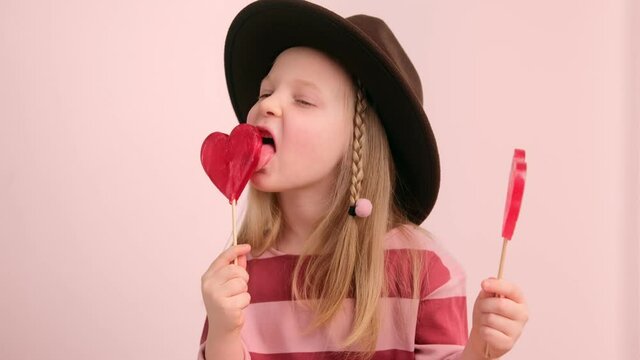 Little girl child eating licks sweet heart shaped candy. Valentine's day concept.