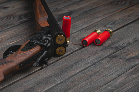 Close-up shot of an old vintage double-barreled shotgun with triggers on a wooden background, three cartridges lying next to it, soft focus