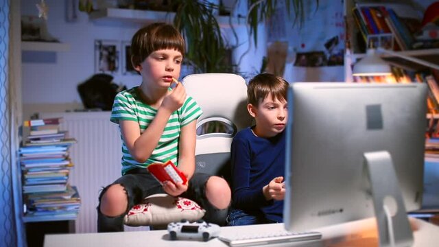 Leisure of free teenagers at home. The boy is eating snacks, looking at the monitor. A teenager uses a joystick in a computer game. Camera movement in the room.