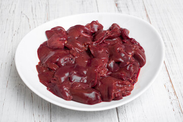 Raw chicken liver on a plate. On a white wooden background.