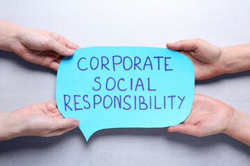 People holding speech balloon with phrase Corporate Social Responsibility on light grey background, top view