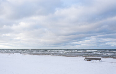 Winter landscape on the coast of the Gulf of Riga with an empty beach bench.