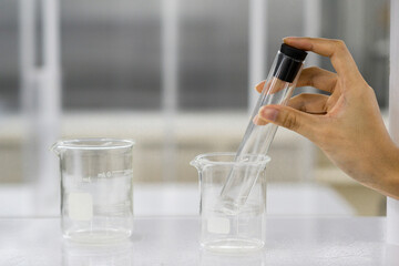 Female hand holding glass tube in beaker on white table on science laboratory background.