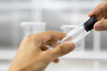 Female hand holding glass tube on science laboratory background.