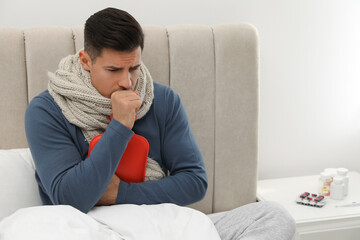 Ill man with hot water bottle coughing at home