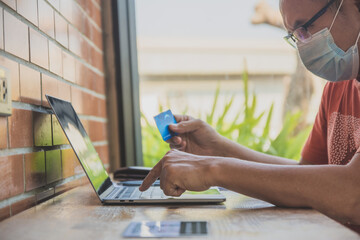 Asian man wear face mask sitting in cafe and shopping online by credit card with laptop online technology