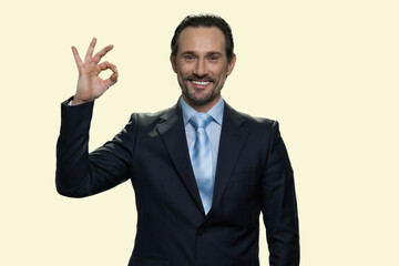 Cheerful middle-aged businessman showing ok gesture. Sign good isolated on yellow background.