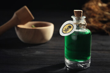 Bottle with poison on black wooden table. Space for text