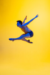 Fototapeta na wymiar Bird's freedom. Young and graceful ballet dancer on yellow studio background in neon light. Art, motion, action, flexibility, inspiration concept. Flexible caucasian ballet dancer, moves in glow.