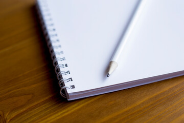 A white notebook and a white pencil on a wooden table. Close-up of a notebook and pencil.