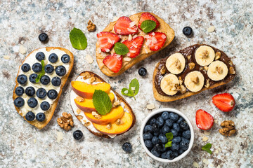 Sweet toast assortment. Chocolate banana, cream cheese and peach, peanut butter and strawberry, cream cheese and blueberry toasts. Stone background, top view.
